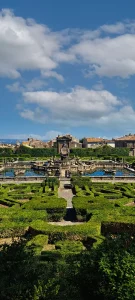 View of Villa Lante gardens with a central fountain intricate hedges and historical buildings under a clear blue sky