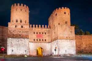 Night view of Porta San Sebastiano an ancient Roman gate along Via Appia Antica illuminated against the dark sky
